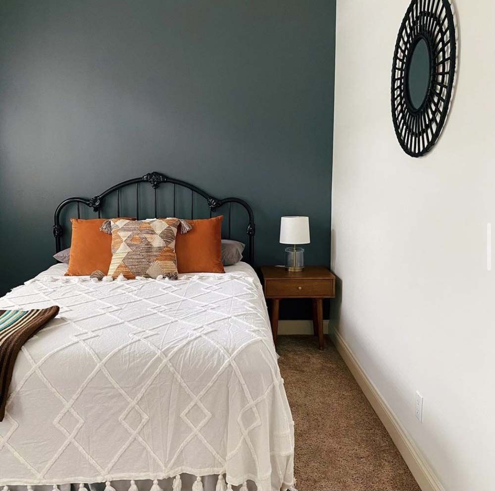 Bedroom with teal accent wall, white bedding, orange pillows, and a black metal headboard.