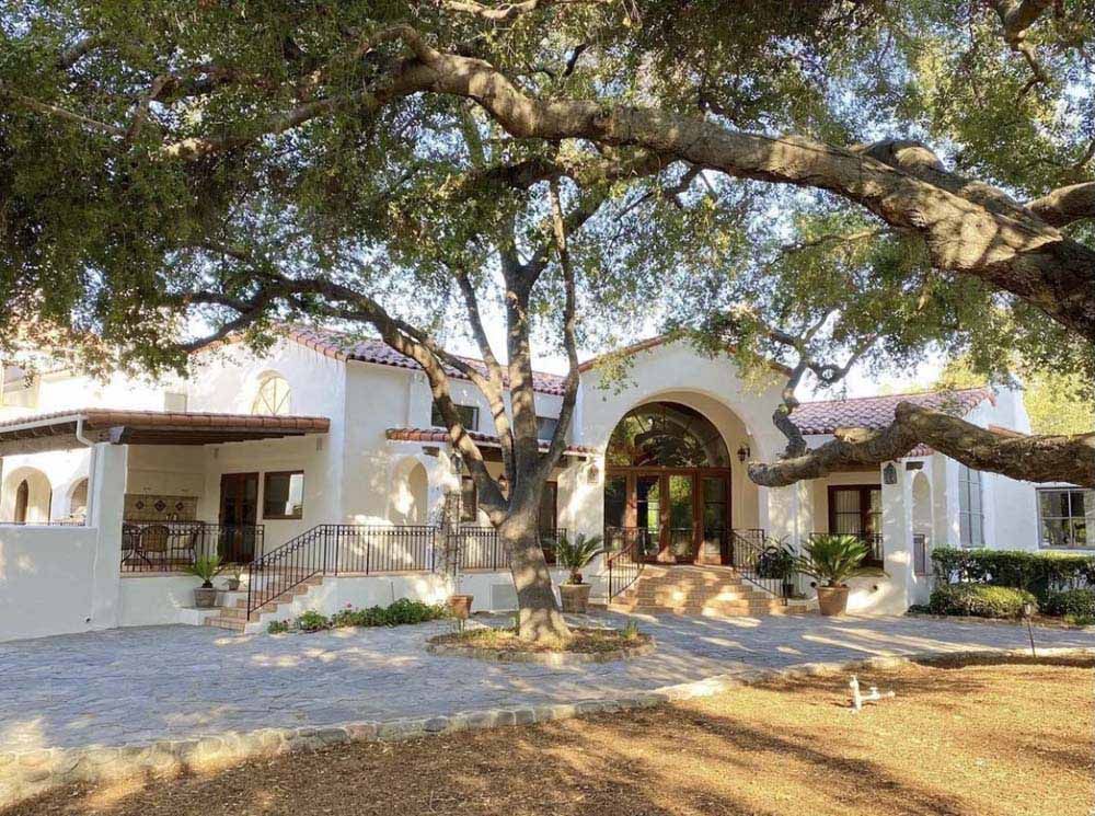 White stucco house framed by large oak tree branches.