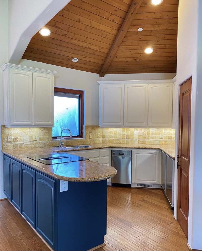 Kitchen with white and blue cabinets, wood ceiling, and granite countertops.