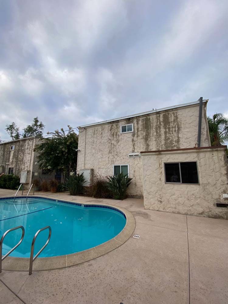 Poolside apartment building with stained exterior under cloudy sky.
