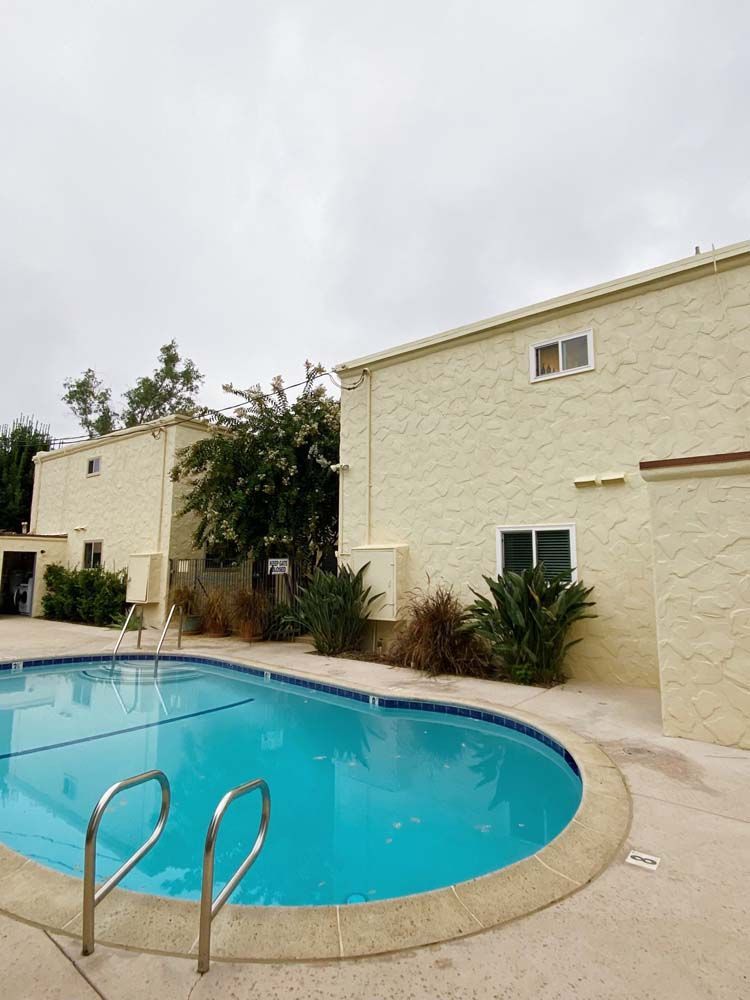 Swimming pool in front of two-story buildings, under a cloudy sky.