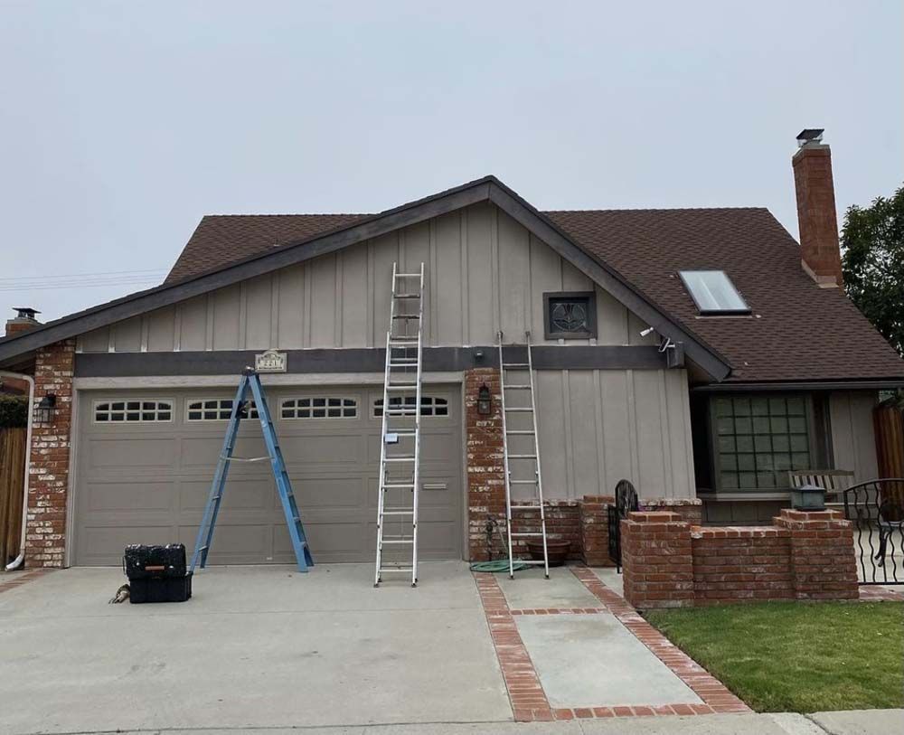 House exterior with ladders propped against the building, likely during a construction or repair project.