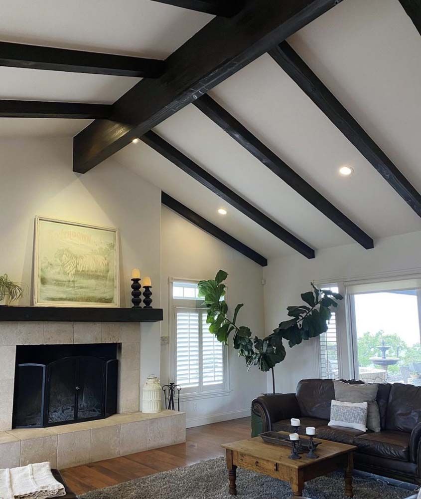 Living room with vaulted ceiling, dark beams, fireplace, and leather sofa.