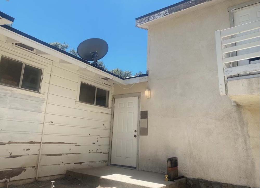 Exterior view of a building with white walls, a door, windows, and a satellite dish against a blue sky.
