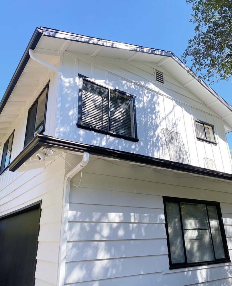 White two-story house with black trim, windows, and garage door under a clear blue sky.