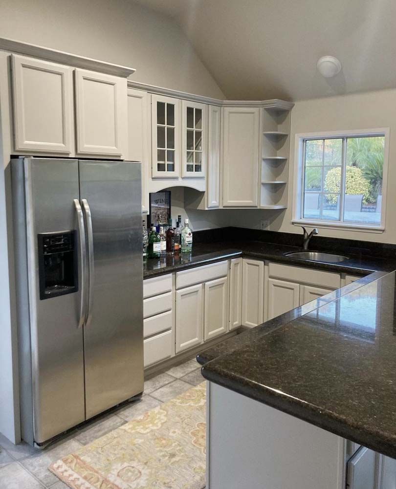 Kitchen with cream cabinets, black countertops, stainless steel fridge, and an island.