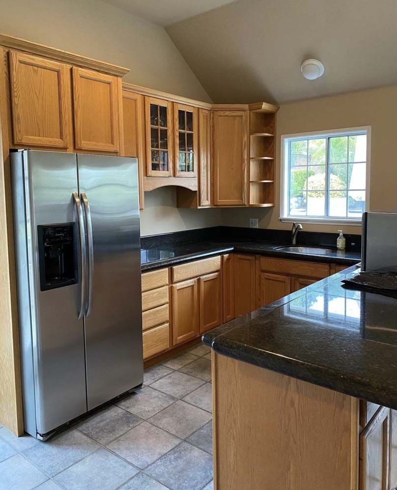 Kitchen with stainless steel refrigerator, wooden cabinets, and granite countertops.
