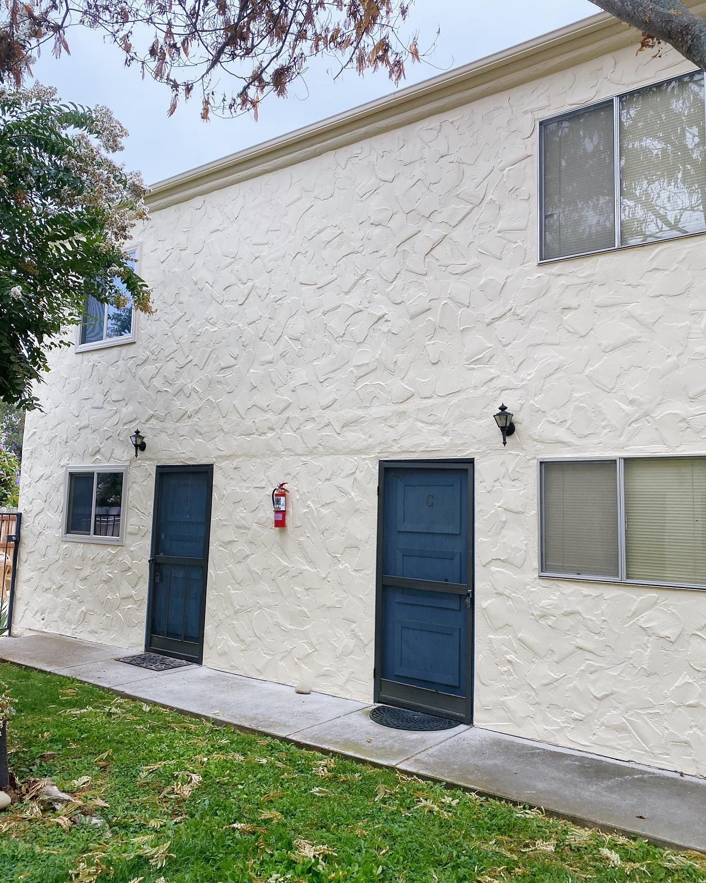Two-story stucco building with blue doors, windows, and a fire extinguisher on the wall.