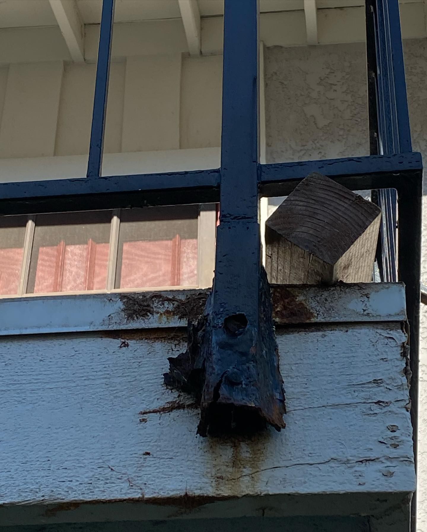 Decayed railing post attached to a weathered wooden structure, with a black metal railing and a support block.
