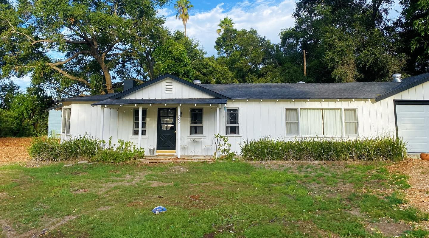 White house with black trim, mint green door, and white picket fence, a driveway with a truck.