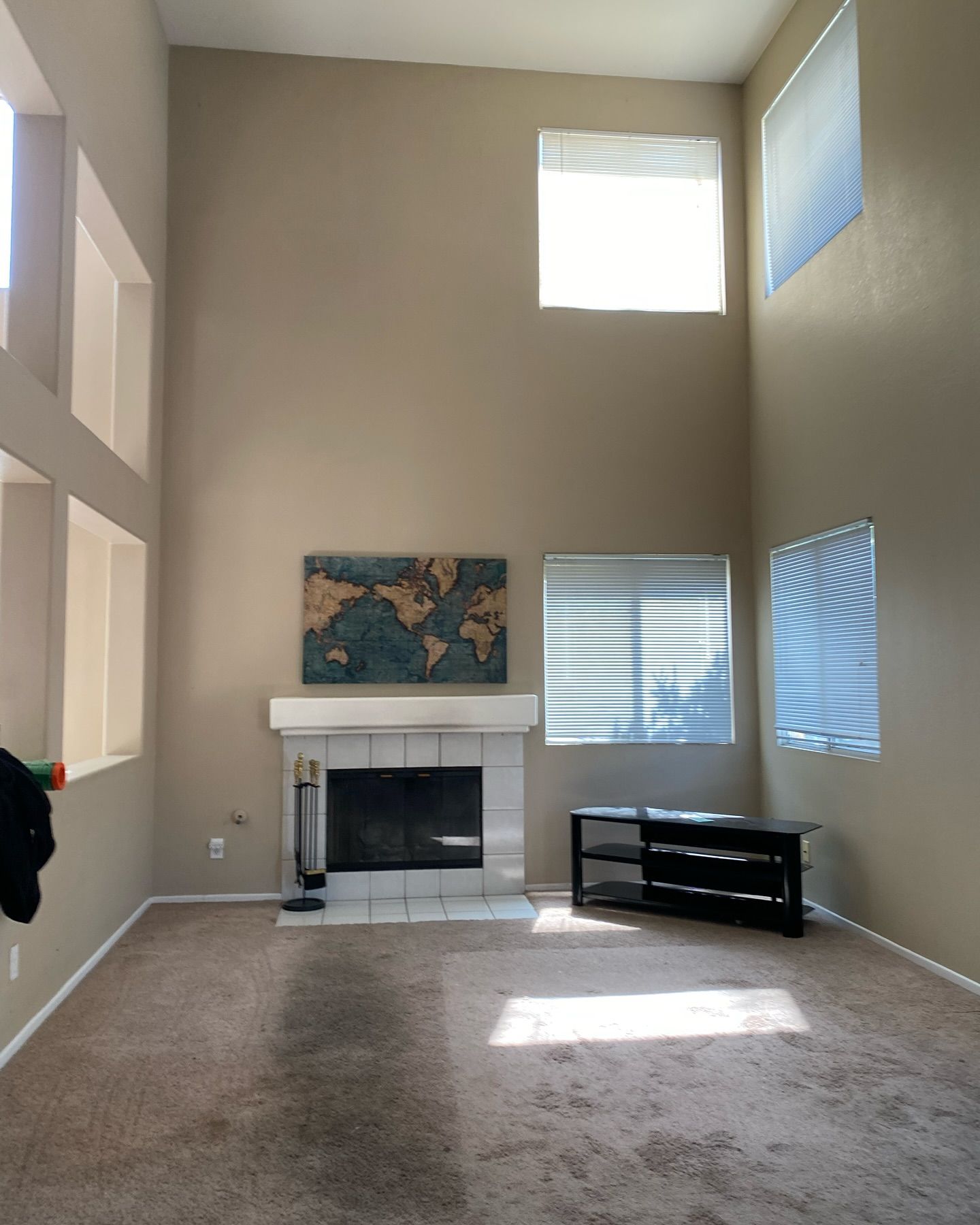 Living room with fireplace, beige walls, and high ceilings. Windows and a world map decor.