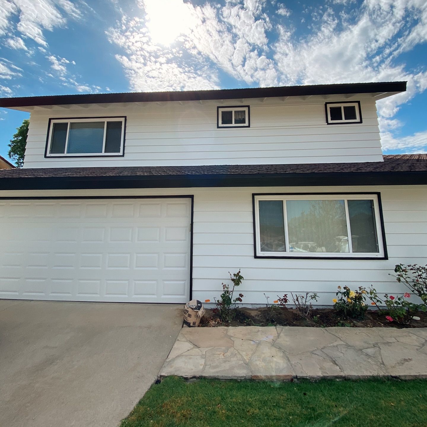 Two-story white house with black trim, blue sky, and a garage door.