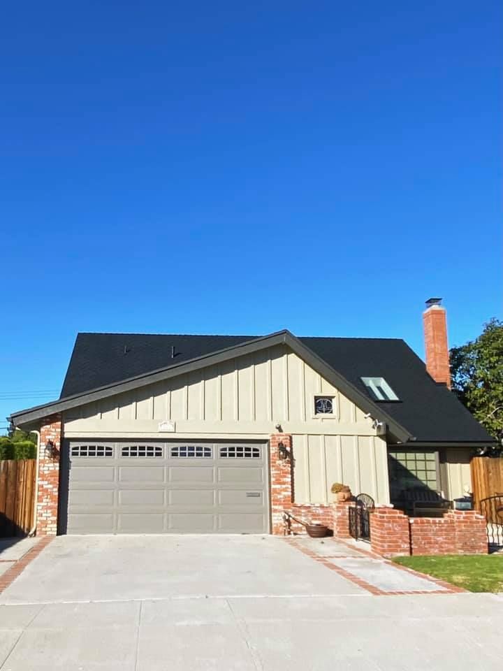 House with a gray garage door, red brick accents, and light-colored siding against a clear blue sky.