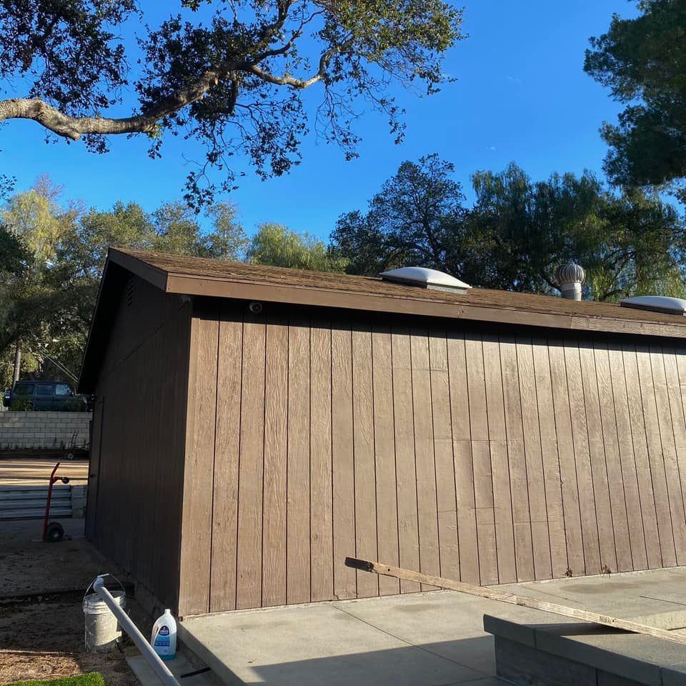 Brown building with textured siding, brown roof, and two skylights against a blue sky.
