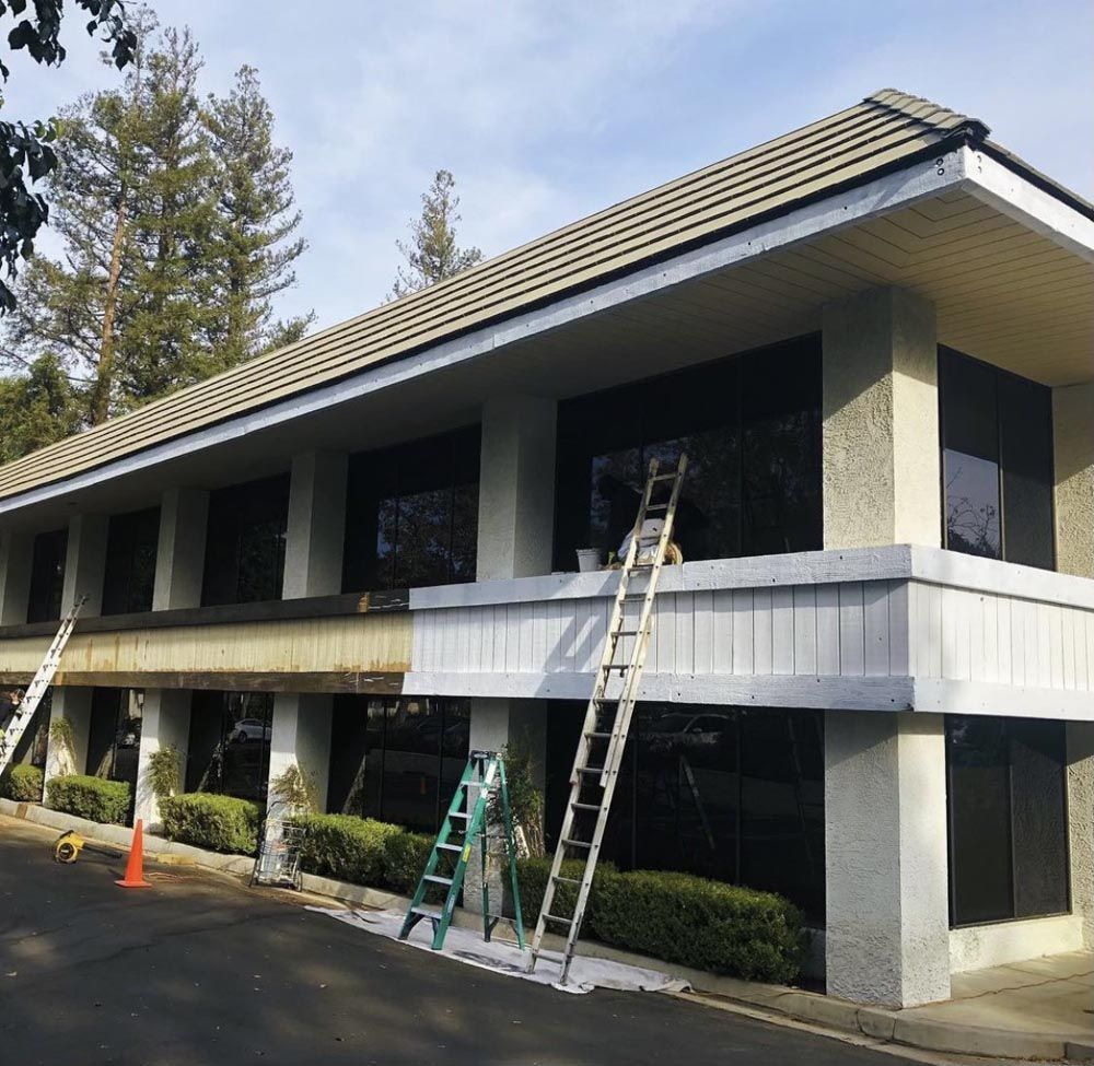 Two-story building with large windows; workers on ladders appear to be cleaning or repairing the exterior.