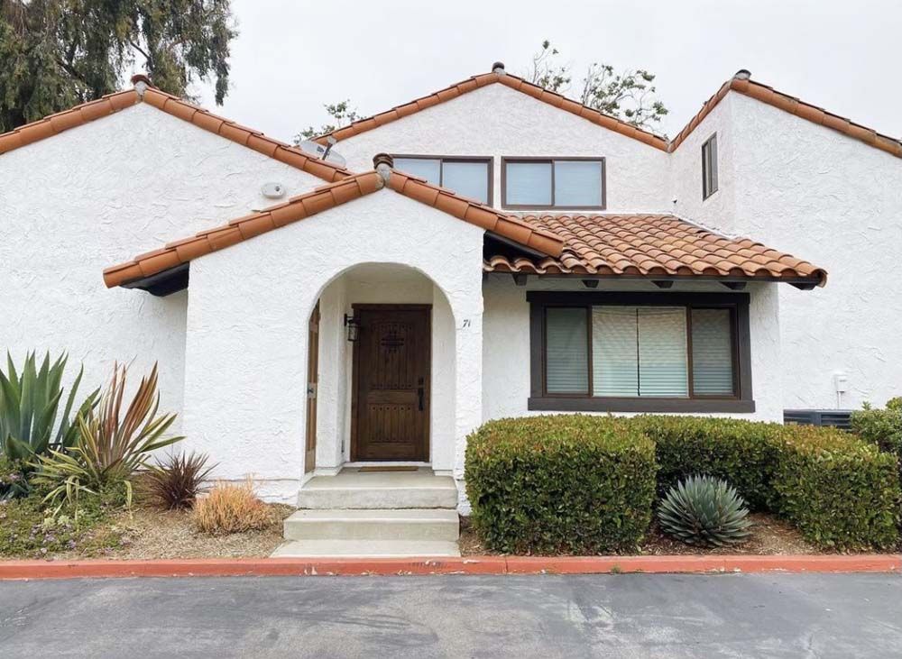 White stucco townhome with terracotta roof and brown trim. Entry door and windows.