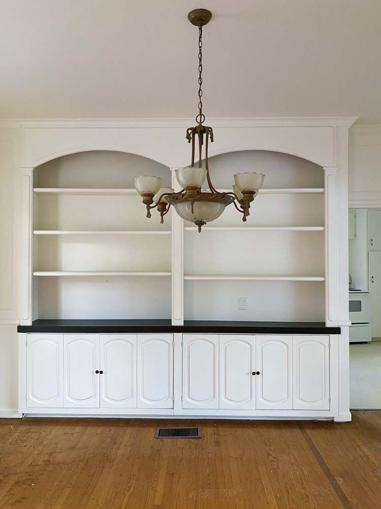 Built-in white bookshelves with cabinets, black countertop, and a chandelier, set against a white wall and wood floor.
