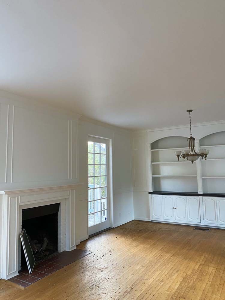 Empty living room with fireplace, built-in shelving, hardwood floors, and a chandelier.