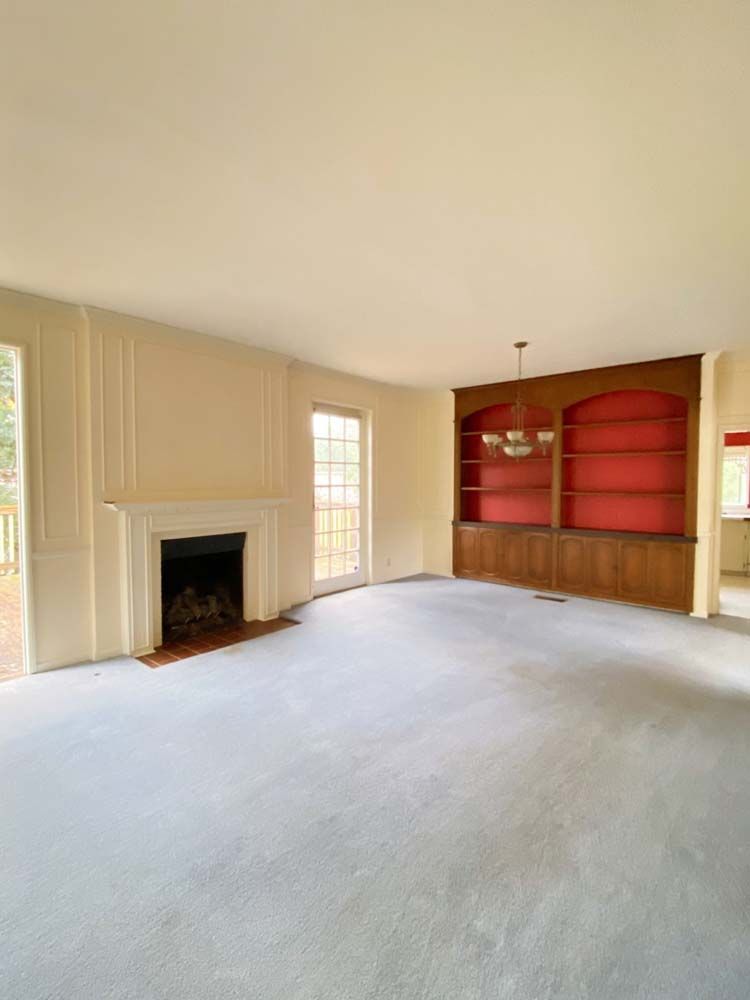 Empty living room with fireplace, built-in shelves (red interior), and light blue carpet.