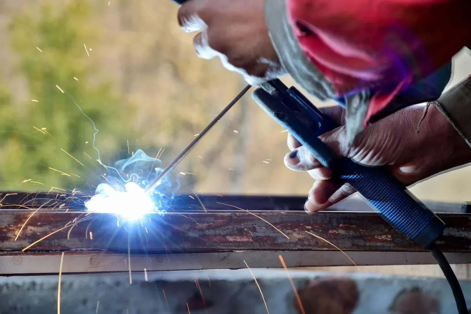 Welder in red sleeve welding metal bar, creating sparks.