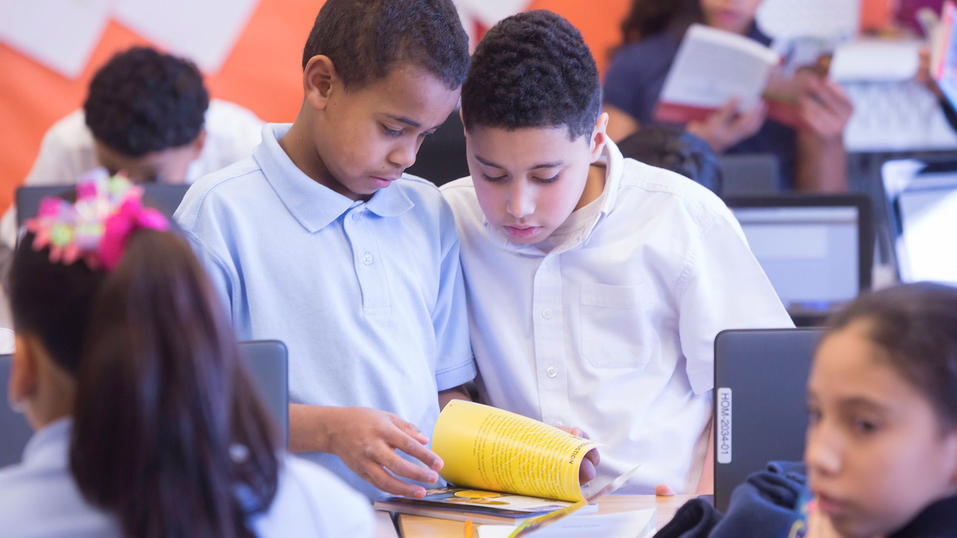Two boys are reading a book together in a classroom