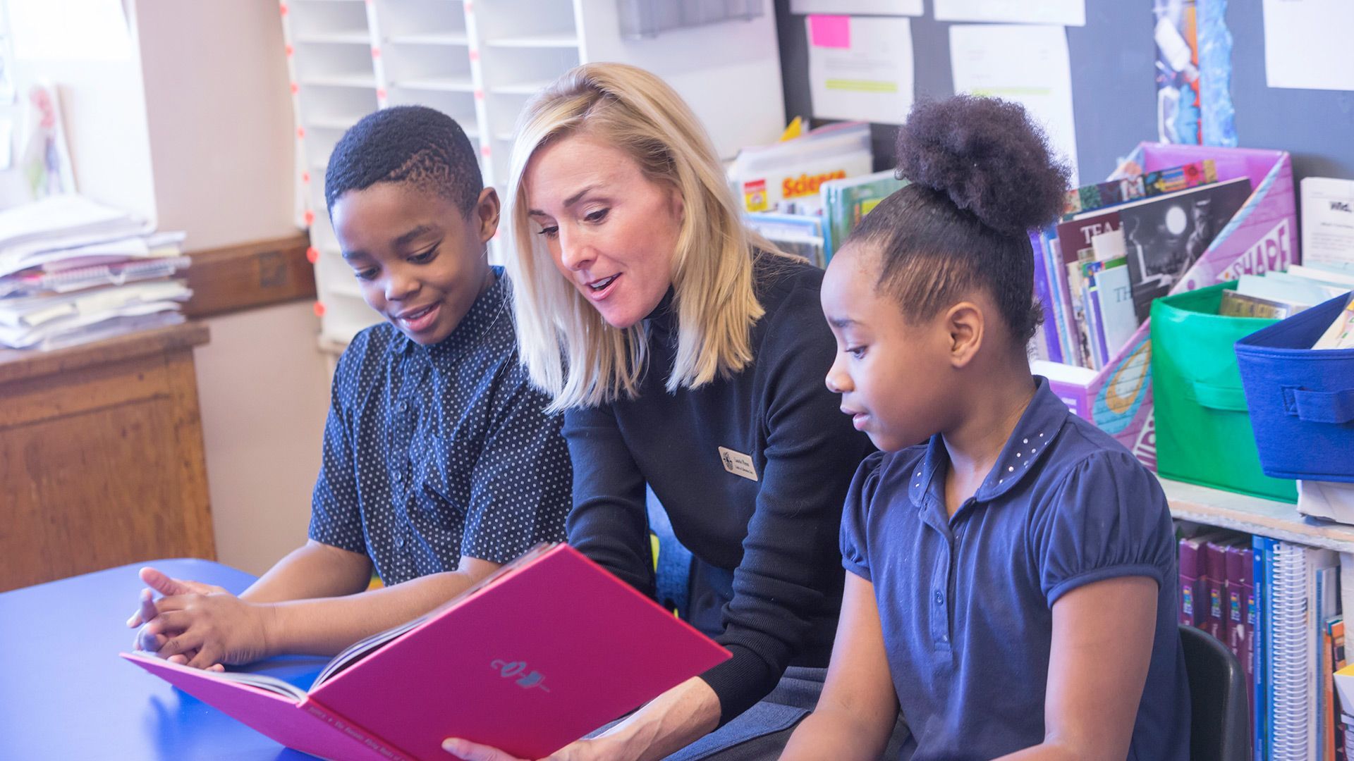 A teacher is reading a book to two children in a classroom