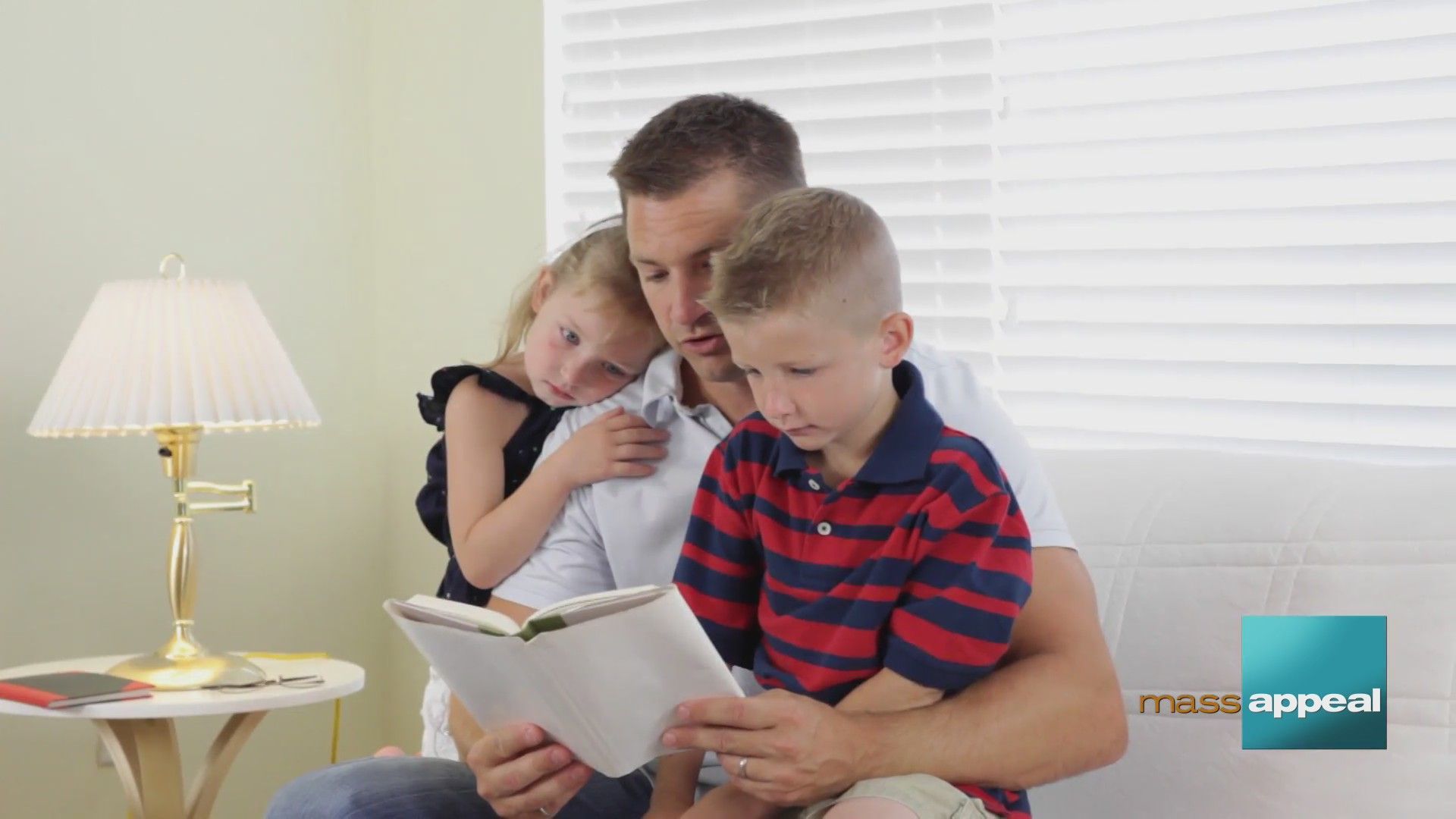 A man sits on a couch reading a book to two children