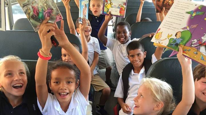 A group of children are sitting on a bus holding books in their hands.