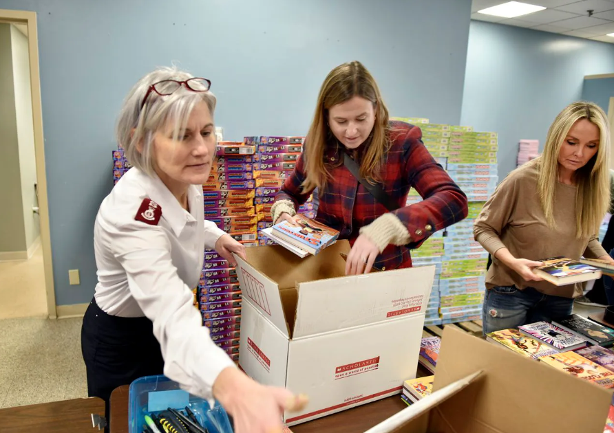 A woman in a military uniform is putting books into a cardboard box