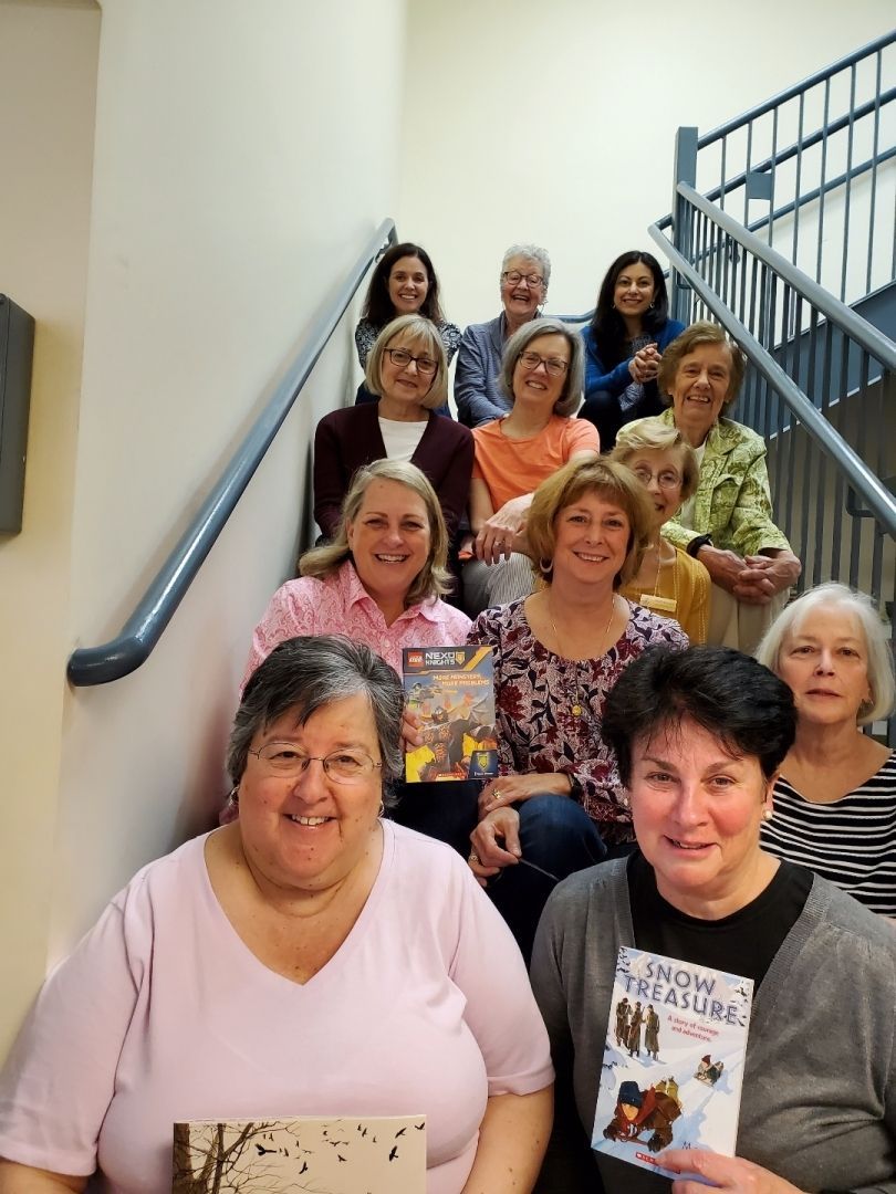 A group of women sitting on stairs holding books including one titled snow vacation
