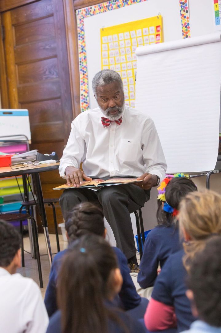 A man in a bow tie is reading a book to a group of children