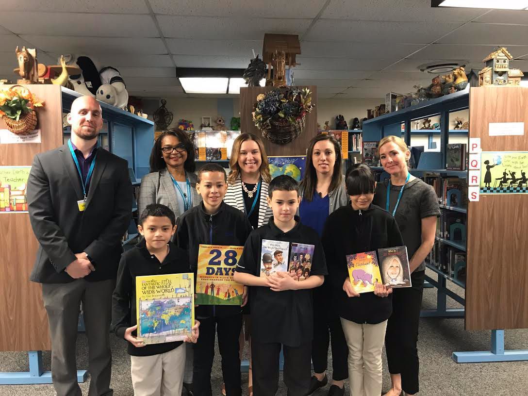 A group of people standing in a library holding books one of which has the number 28 on it