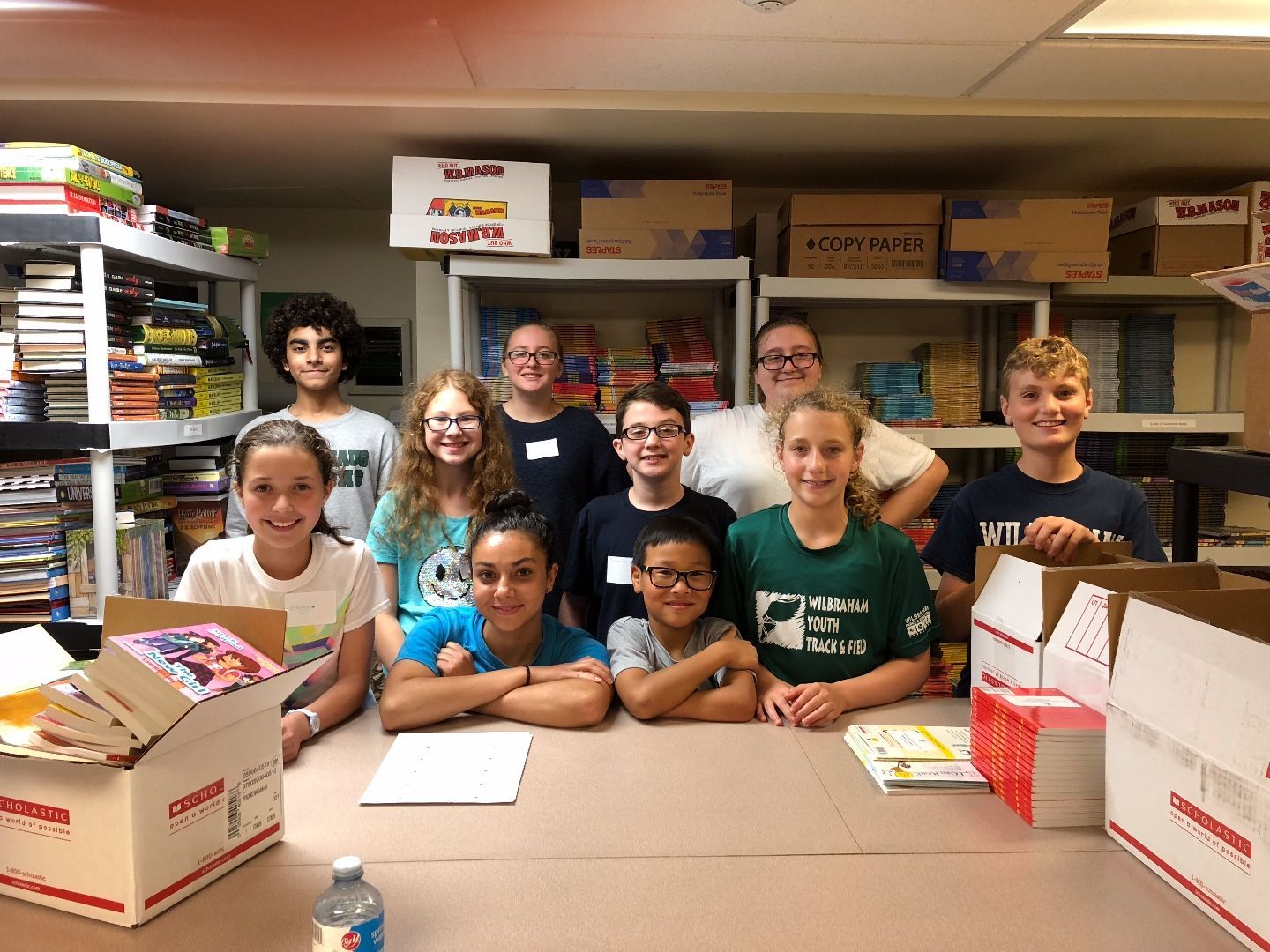 A group of children are posing for a picture in a room with boxes and shelves