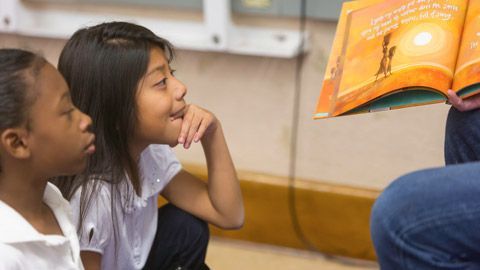 A woman is reading a book to two young girls.