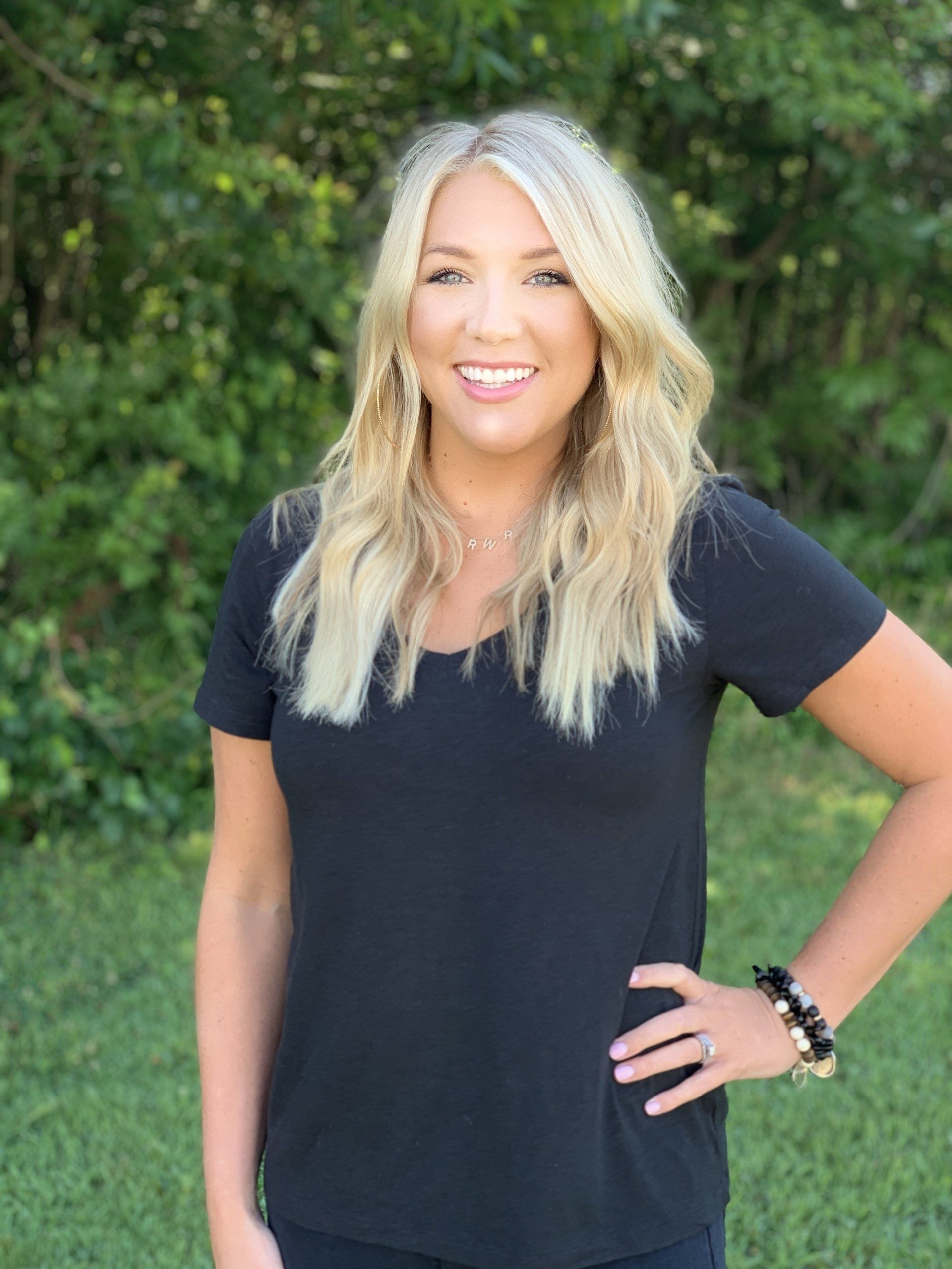 A woman in a black shirt is standing in a field with her hands on her hips.