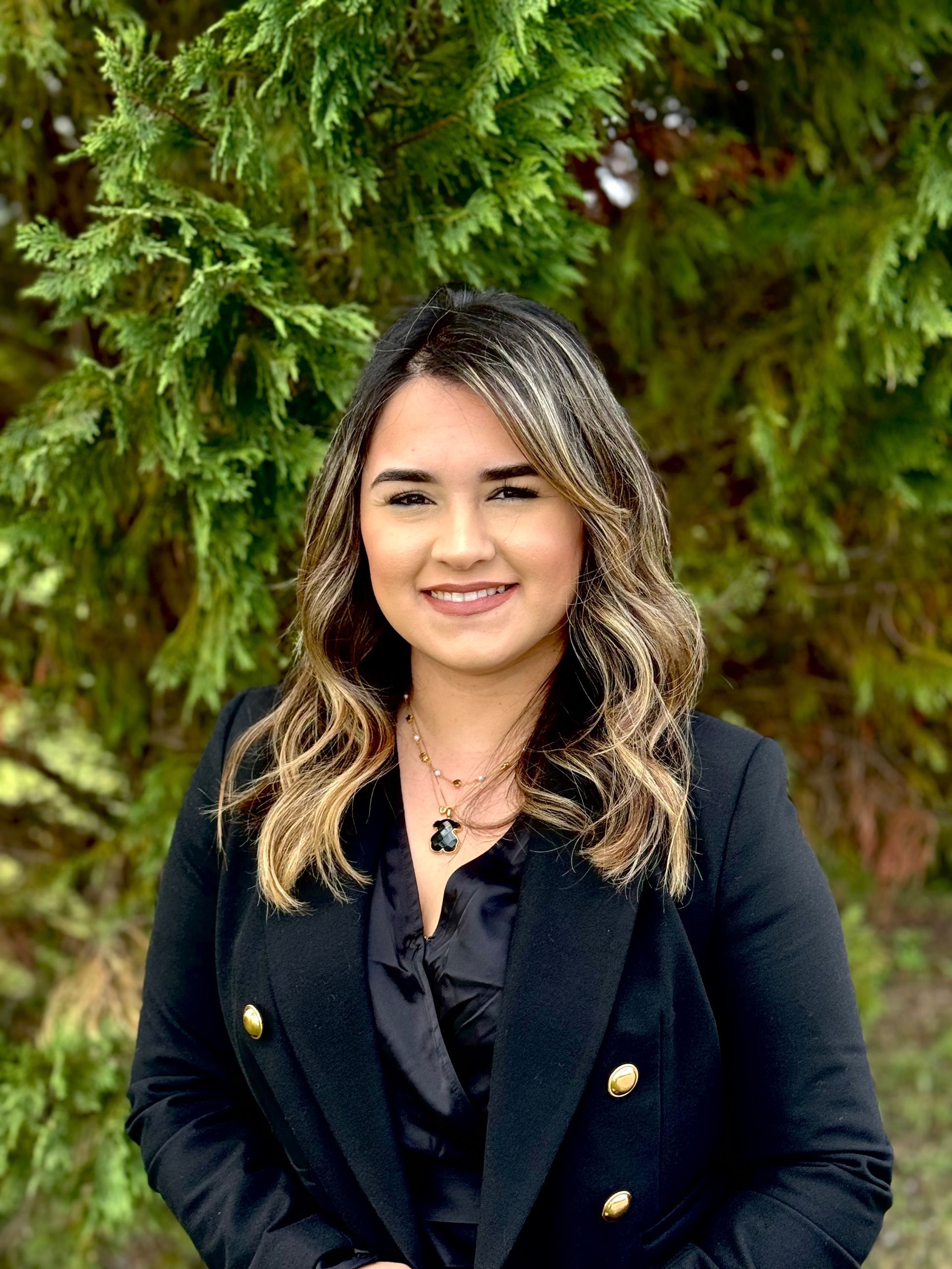 A woman in a black jacket is standing in front of a tree.