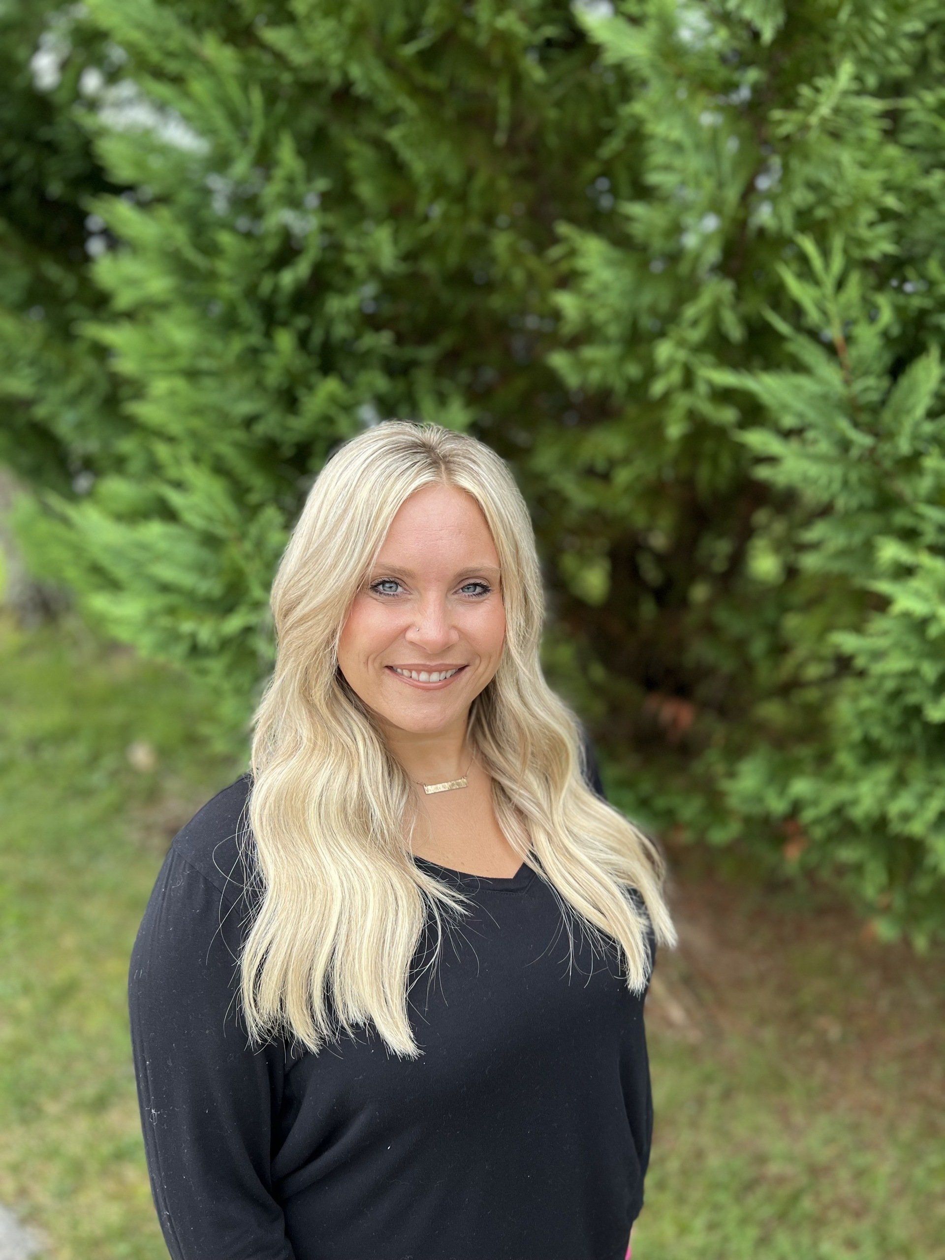 A woman in a black shirt is standing in front of a tree.