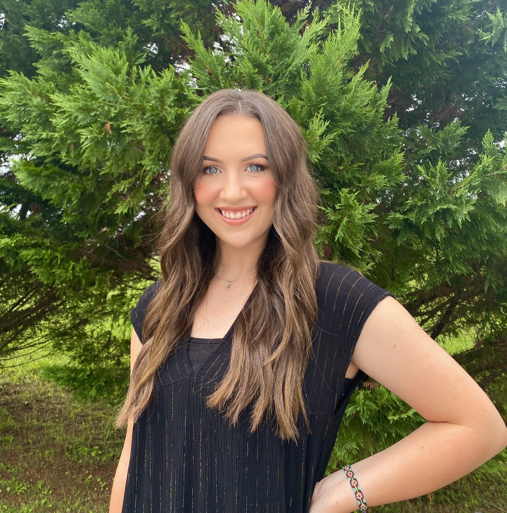 A woman in a black shirt is smiling in front of a tree.