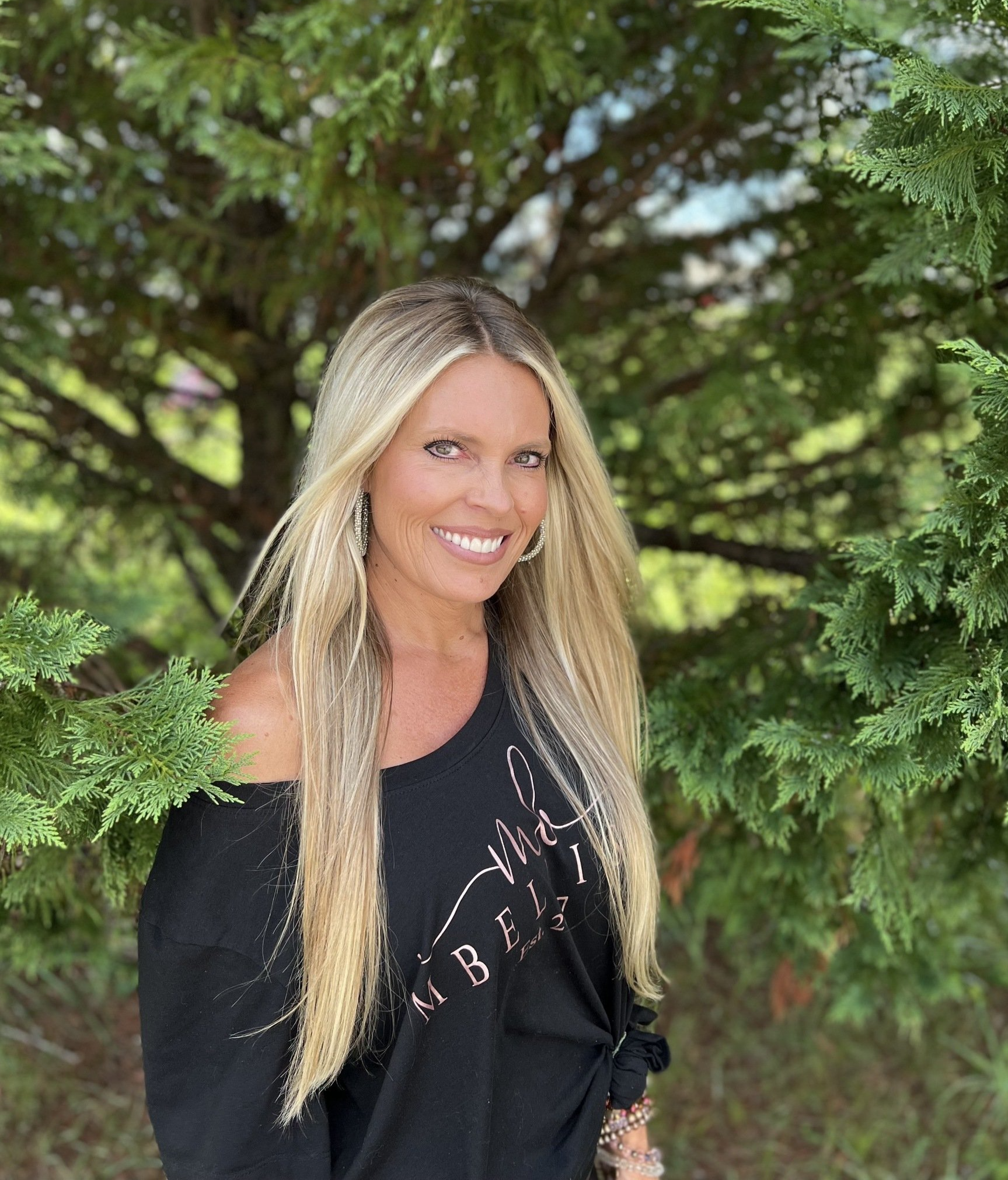 A woman in a black shirt is standing in front of a tree.