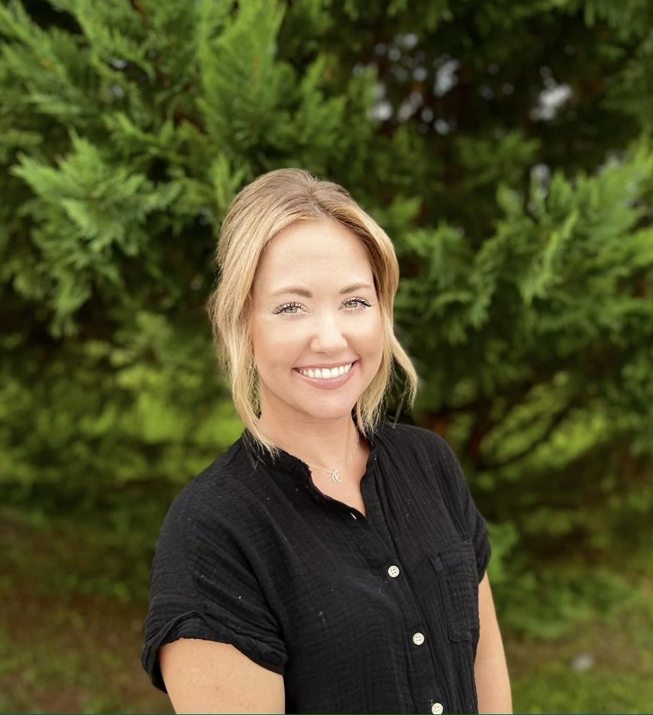 A woman in a black shirt is smiling in front of a tree.