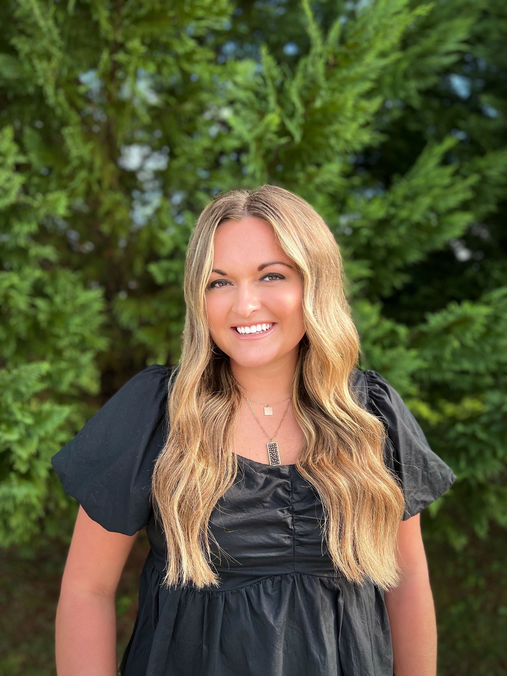 A woman in a black dress is standing in front of a tree.