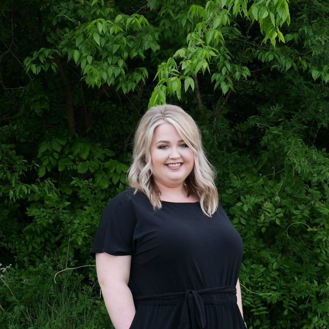 A woman in a black dress is standing in front of a forest.