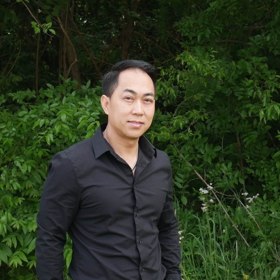 A man in a black shirt is standing in front of trees.