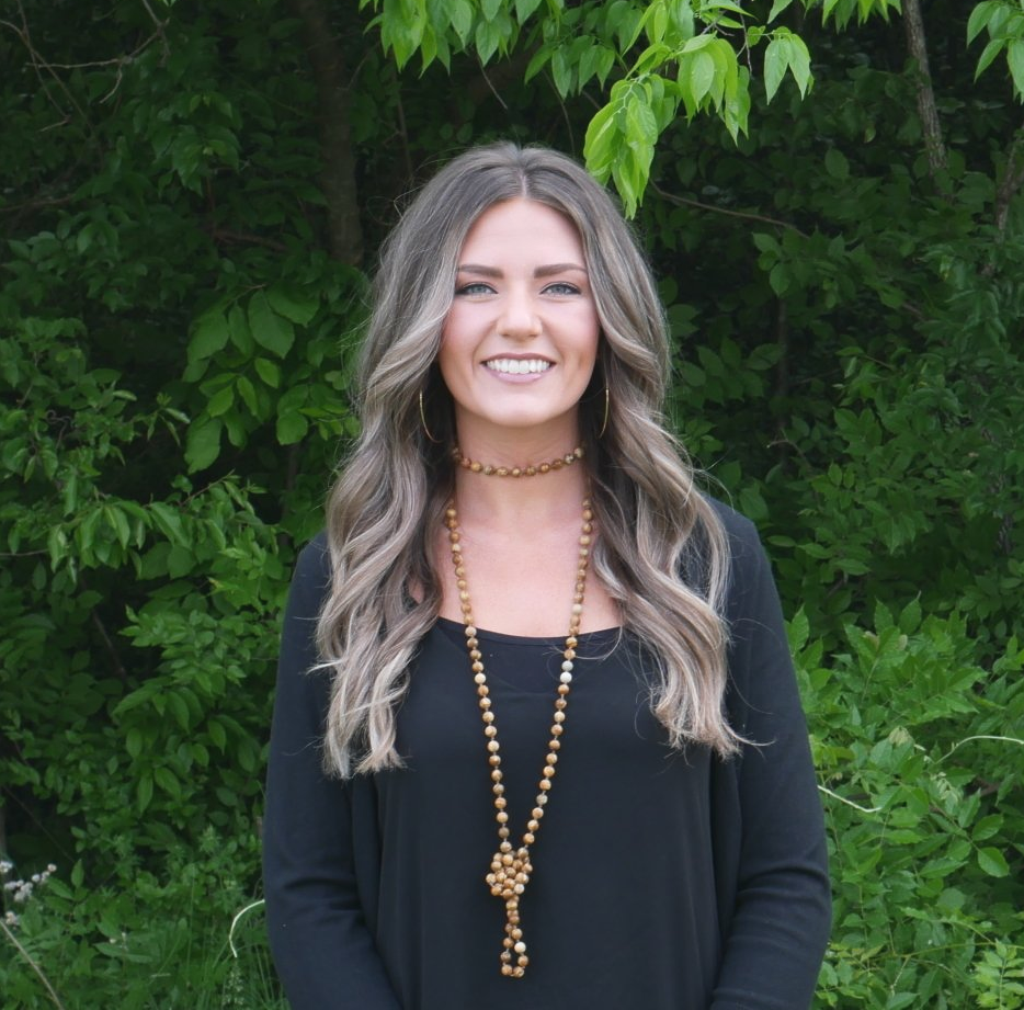 A woman wearing a black shirt and a gold necklace smiles for the camera