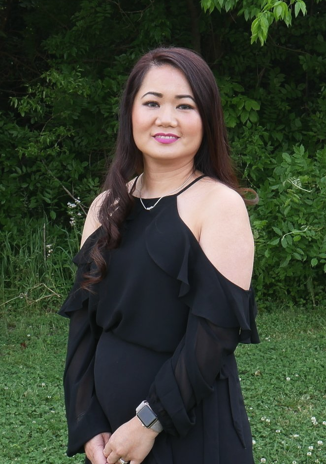 A woman in a black dress is standing in a grassy field.