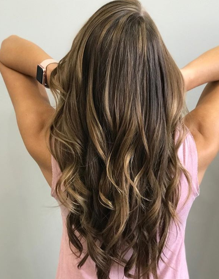 A woman with long brown hair is wearing a pink tank top.