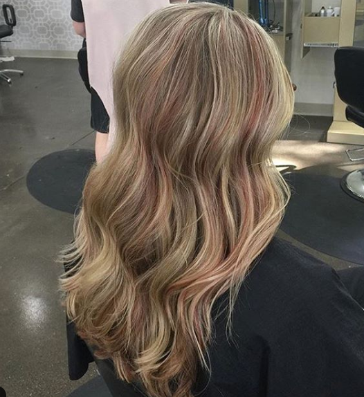 A woman with long blonde hair is sitting in a chair in a salon.