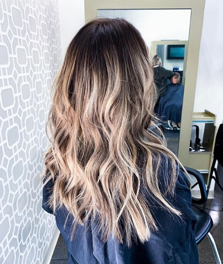 A woman with long hair is sitting in a chair in front of a mirror.