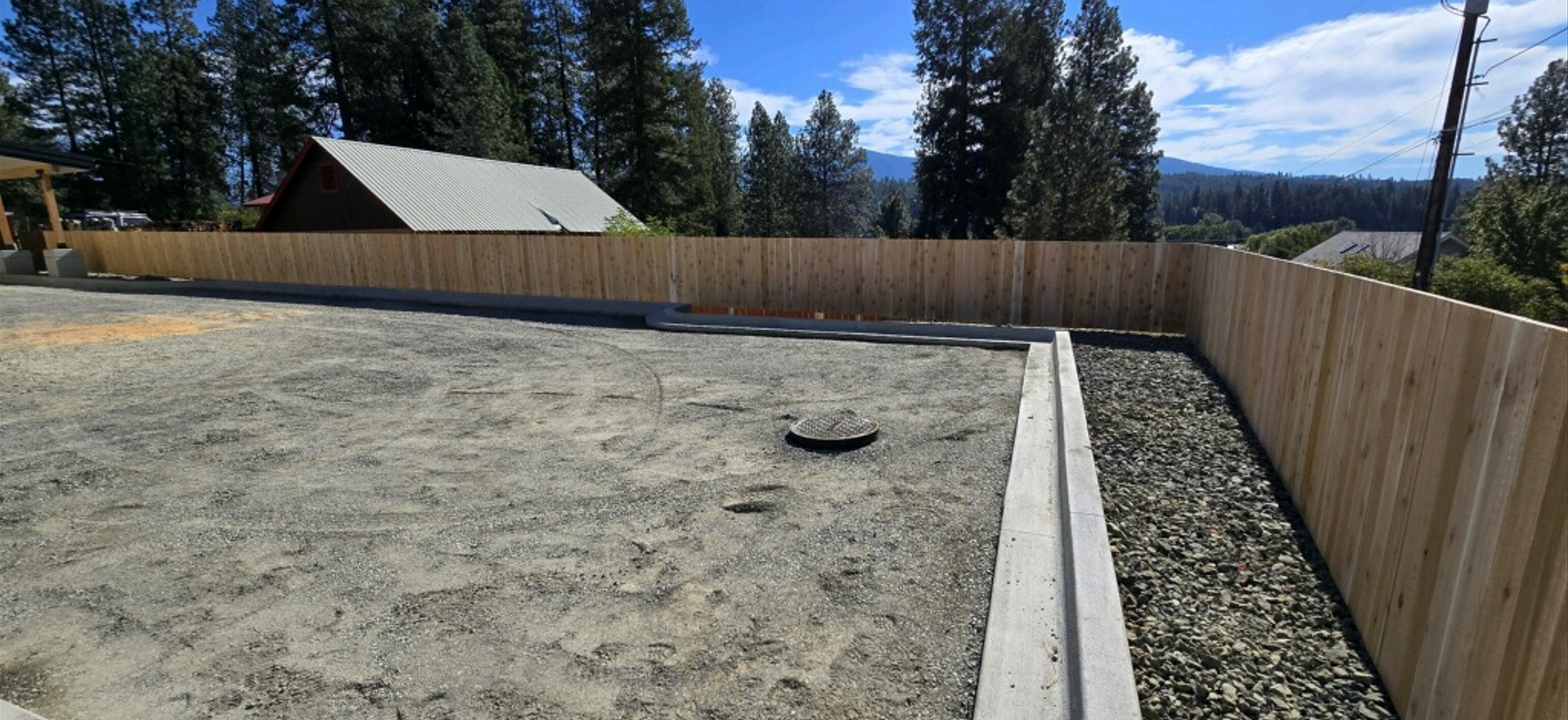 A wooden fence surrounds a dirt yard with a house in the background. Project done by Raise the Bar Construction