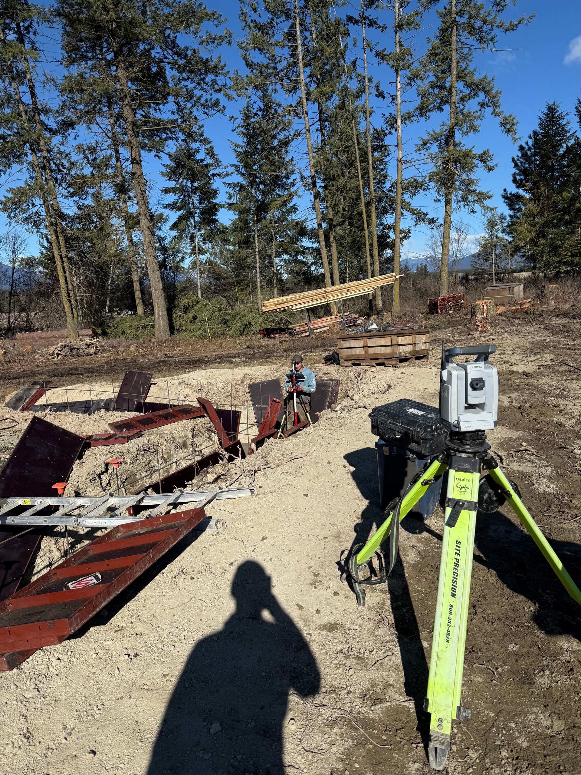A tripod with a camera on it is sitting on top of a dirt field. Project done by Raise the Bar Construction